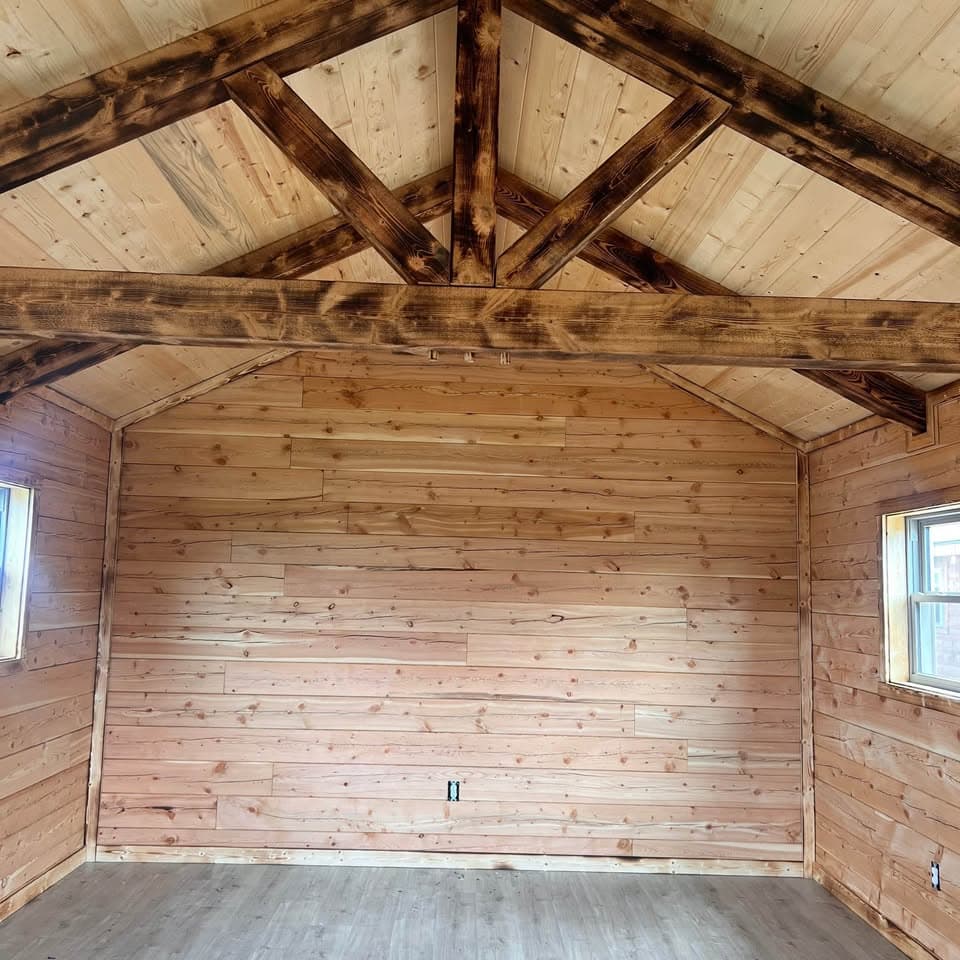 Log cabin interior with vaulted ceiling, dark-stained exposed wooden beams in truss pattern, and natural wood paneling