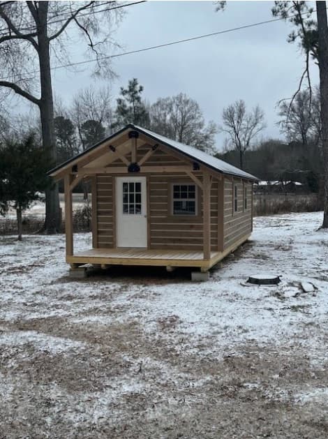 Small chinked log cabin exterior with covered porch in winter setting